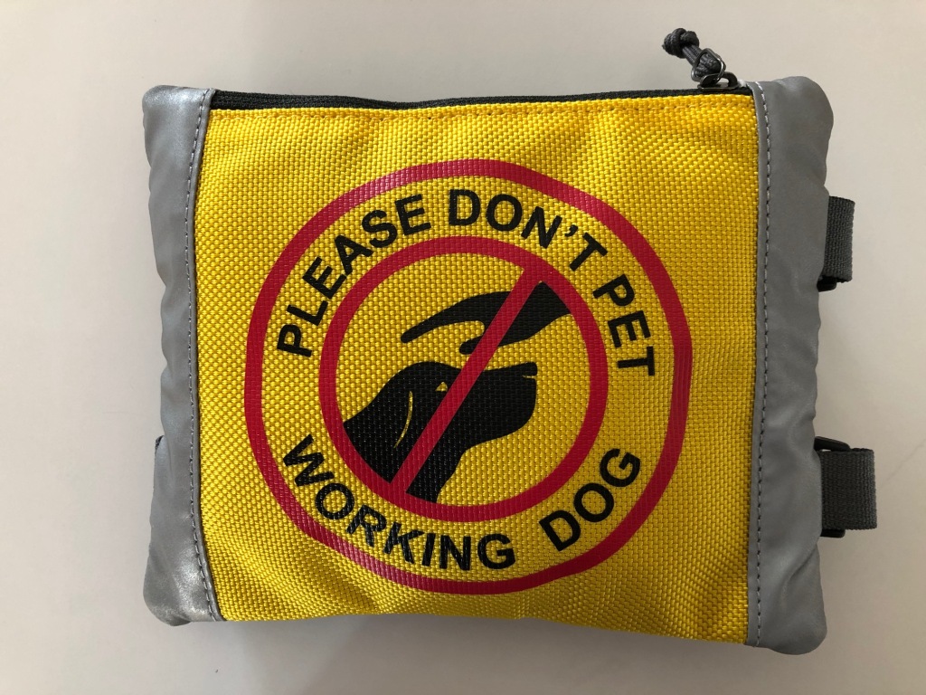 Harness sign, front view. HARNESS SIGN - It fastens to the harness handle with adjustable straps and backpack clips. The sign is bright yellow with black lettering stating “Please don’t pet working dog.” The sign also features a picture of a dog’s head with a hand above it with a red slash through it (the universal “no” sign) for a more visual effect.